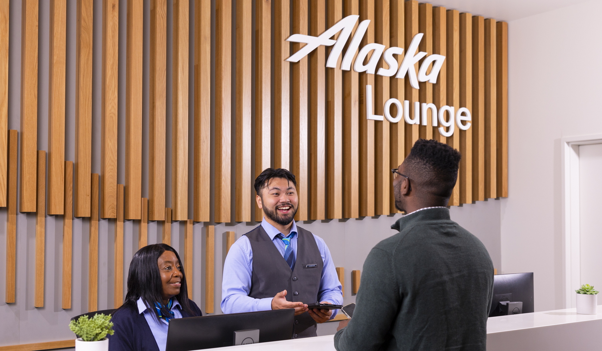 Two customer service agents at Alaska Airlines lounge helping customer.