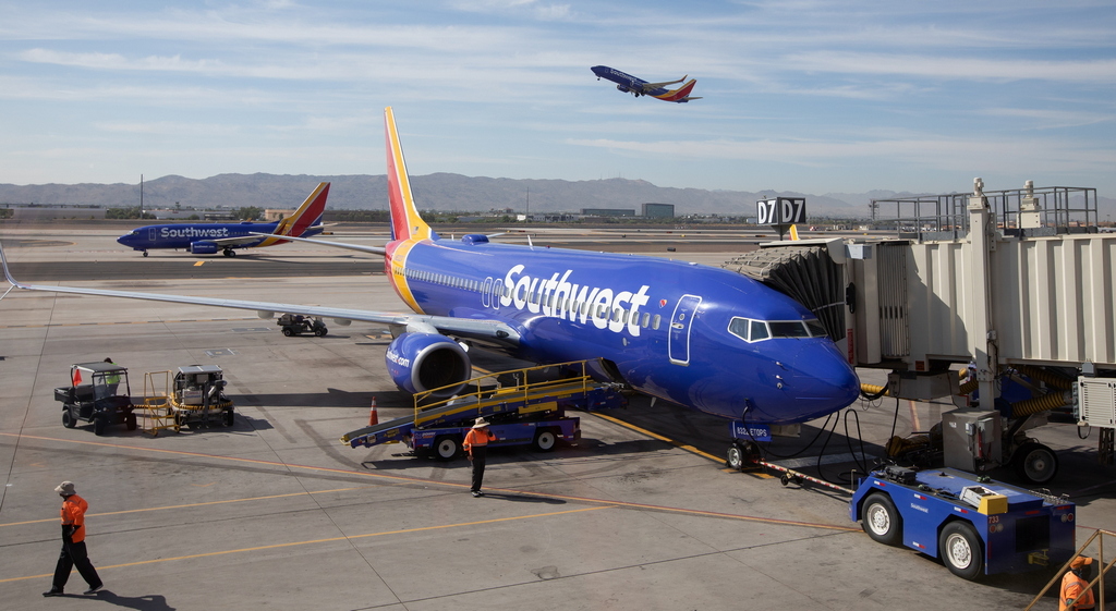 Southwest Airlines plane at gate and plane taking off in background.