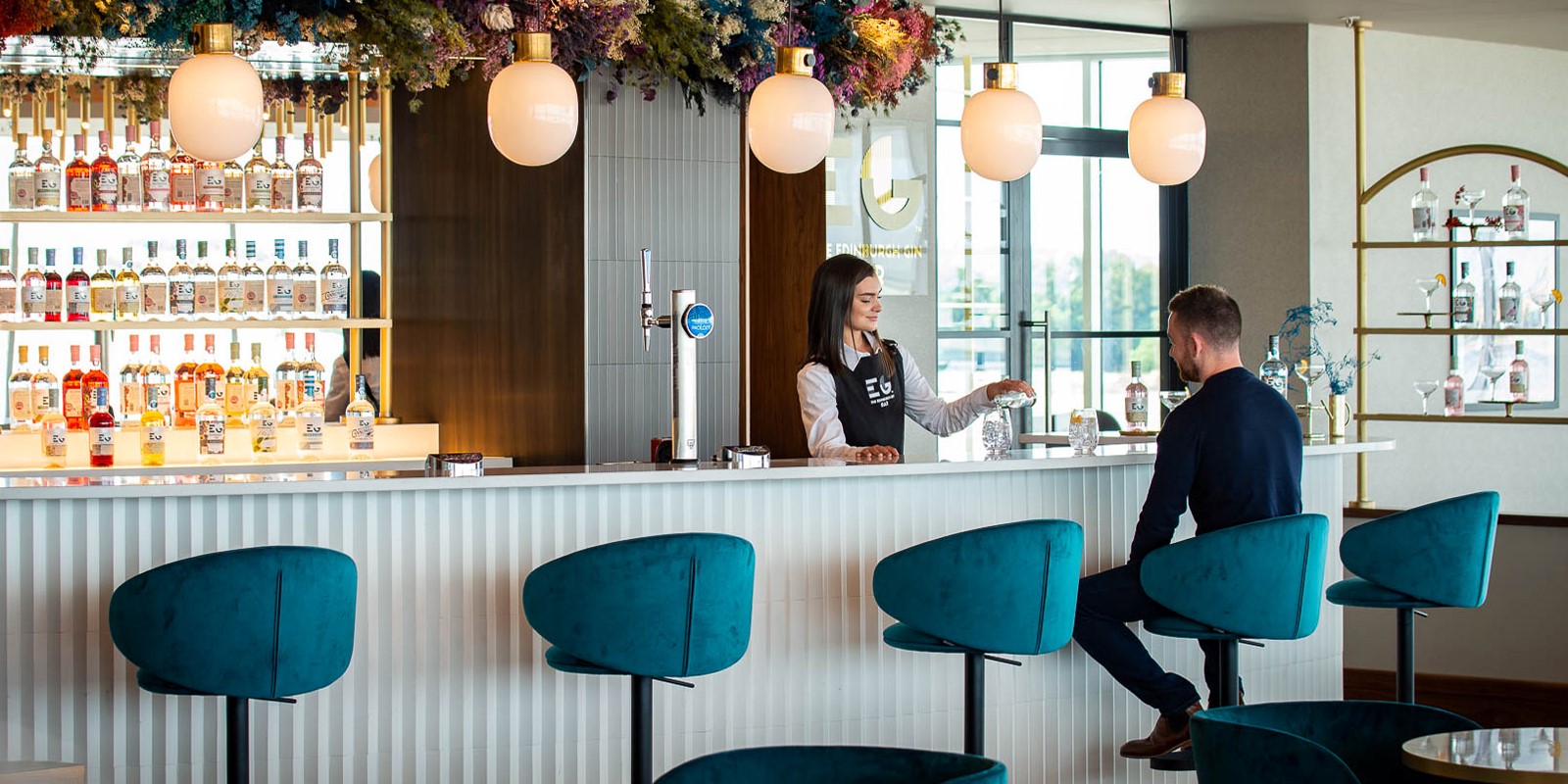 bar area showing a person pouring a drink with a person sitting.