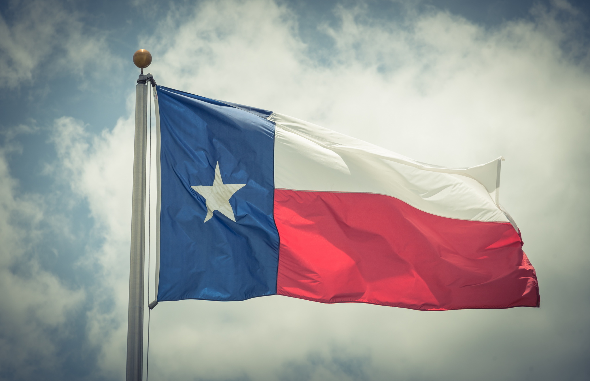 Texas Flag blowing in the wind with cloudy skies behind.