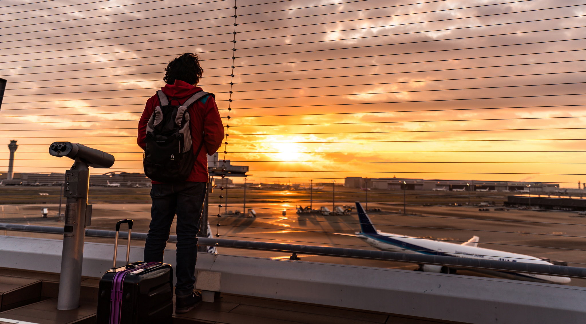 person standing outside at sunset watching a plane at an airport taxi